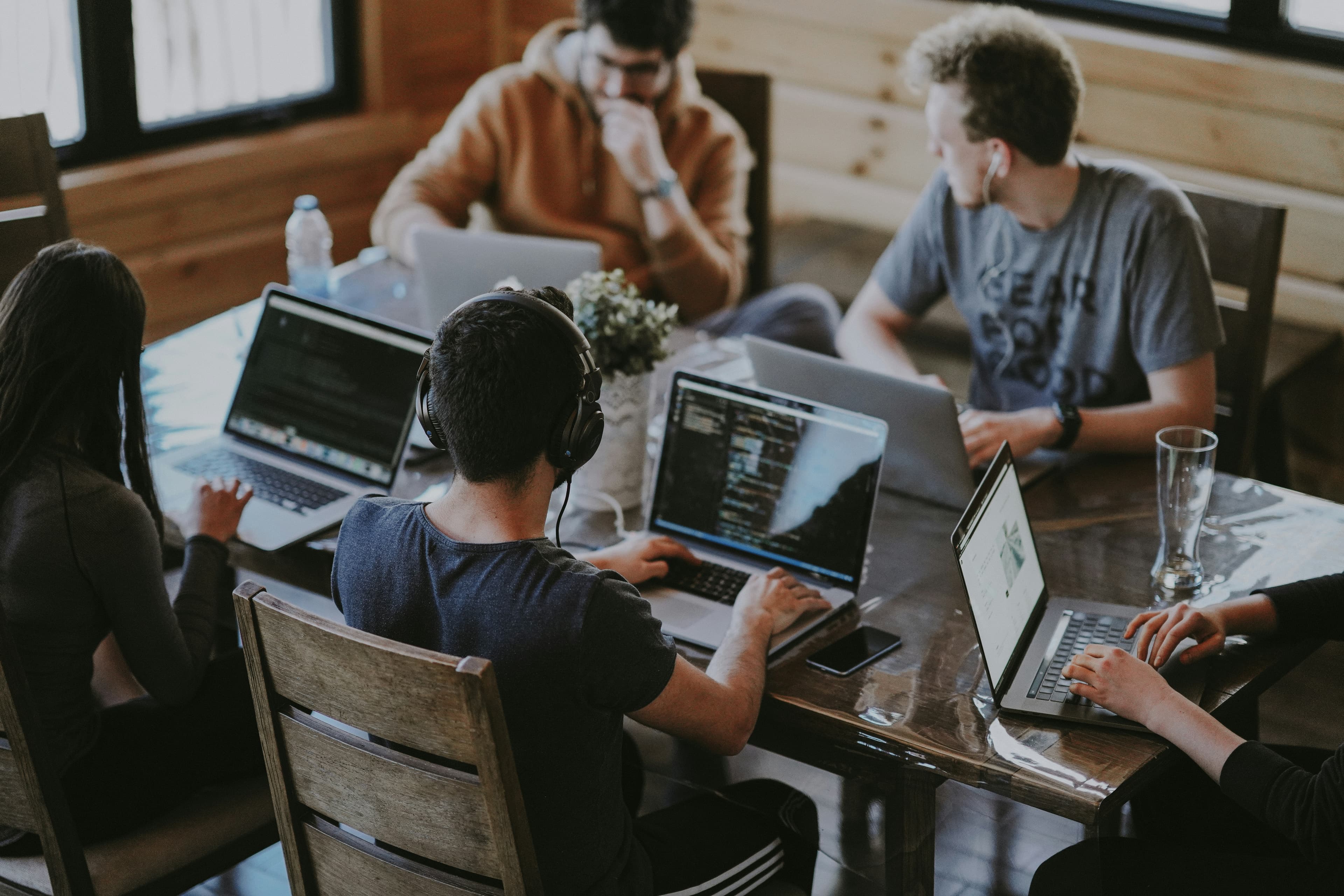 A small team working together around a wooden table covered in laptops.