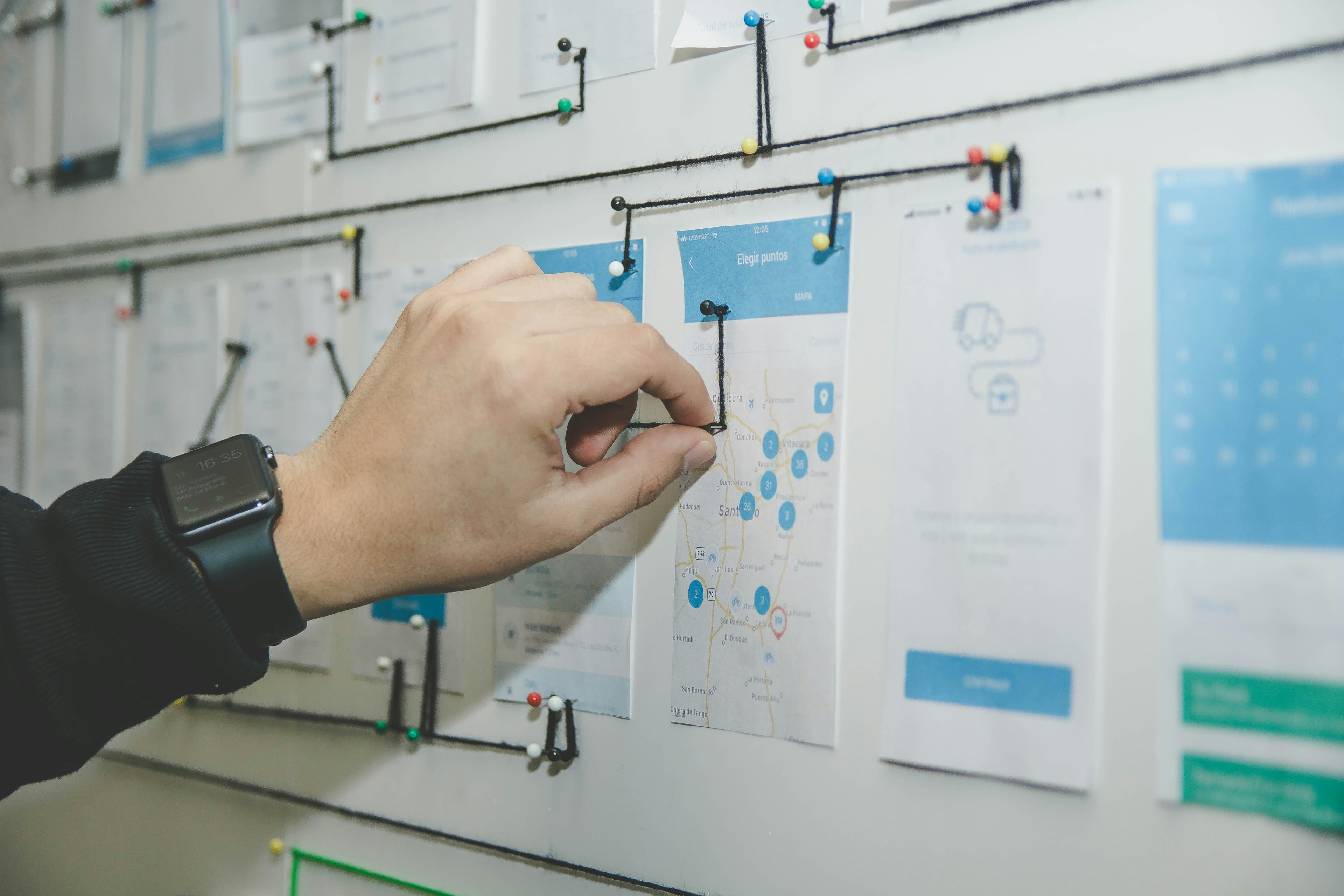 A hand pinning a printed page wireframe to a wall covered in a mapped out site structure.
