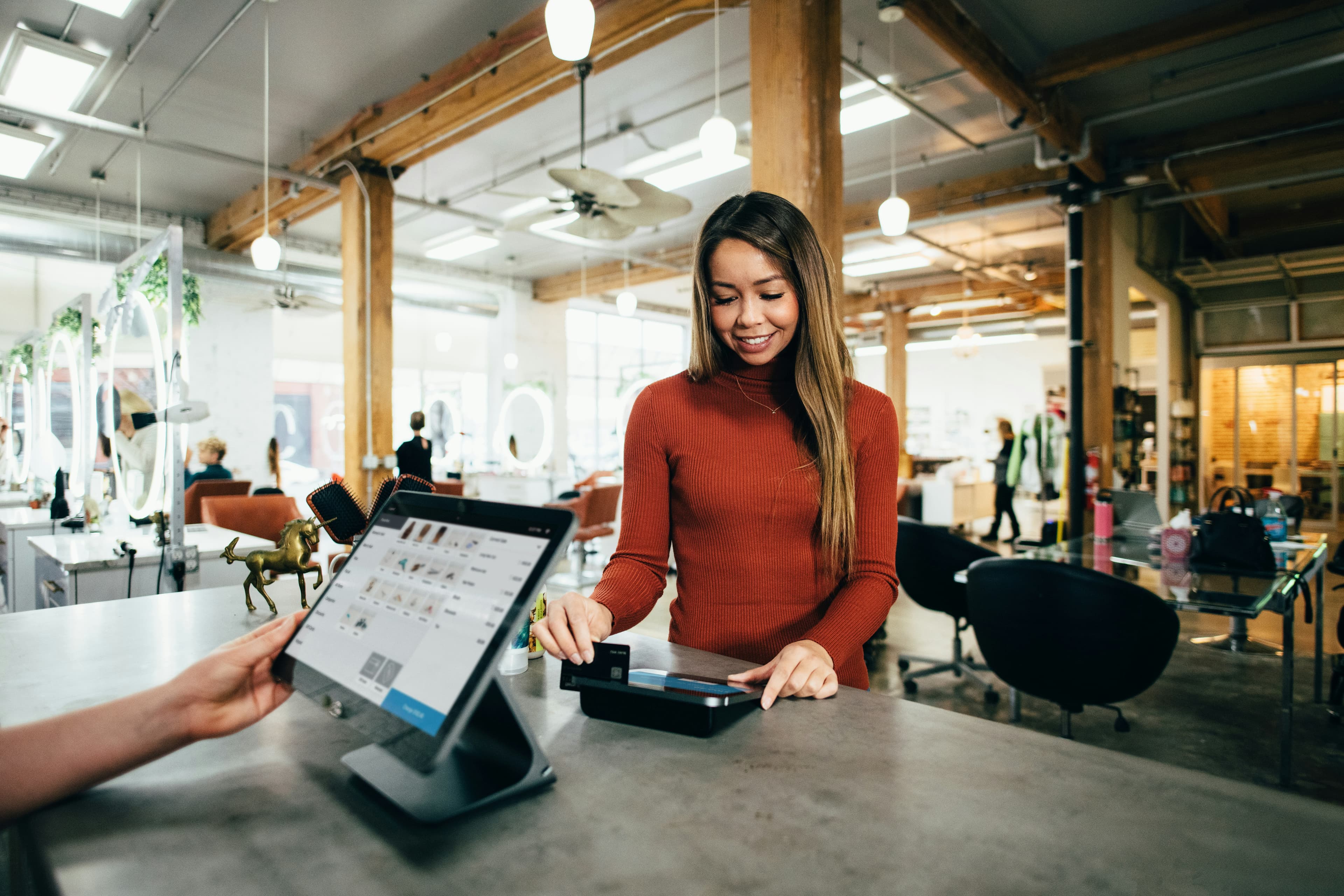 A customer at a shop counter paying while a staff member takes the order on a tablet.